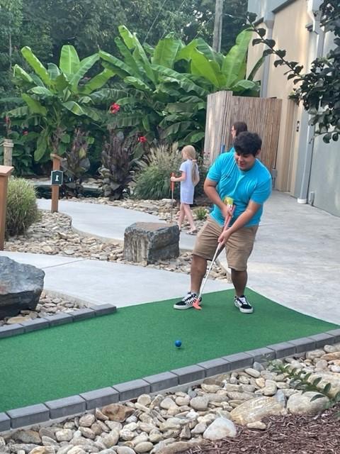 A person playing mini-golf on a green course surrounded by plants.